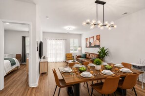 Un espace repas moderne avec une table en bois mise pour le repas, un canapé, un téléviseur et une plante.