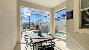Ein überdachter Patio-Bereich mit Tisch und Stühlen, Blick auf einen Pool und ein Schild mit den Poolregeln.