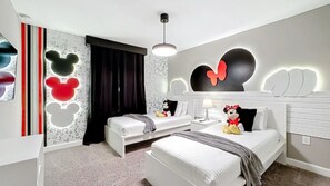 Ein Hotelzimmer mit zwei Betten, einem Bettgestell mit Mickey Mouse Motiv und einem Mickey Mouse Stofftier auf einem Bett.