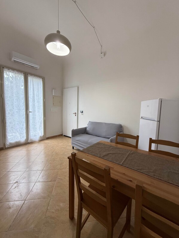 Quarto com mesa de jantar, cadeiras, sofá, luminária no teto e geladeira.