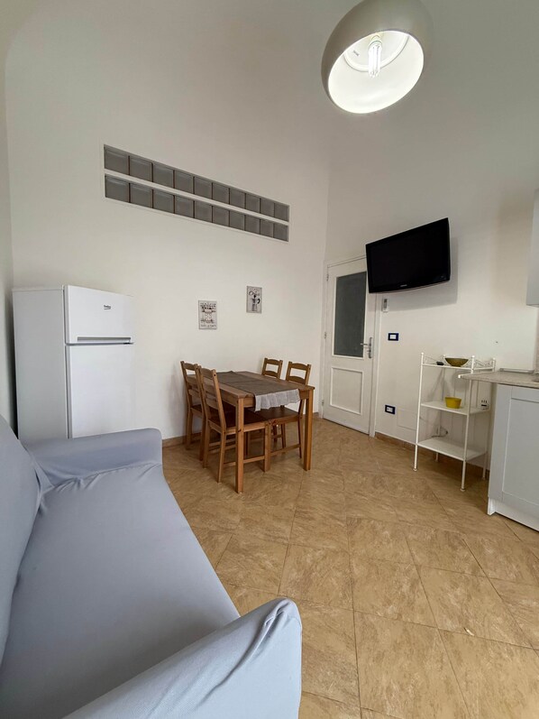 Un espacio habitable compacto con comedor, kitchenette, televisor de pantalla plana montado en la pared y lámpara de techo.