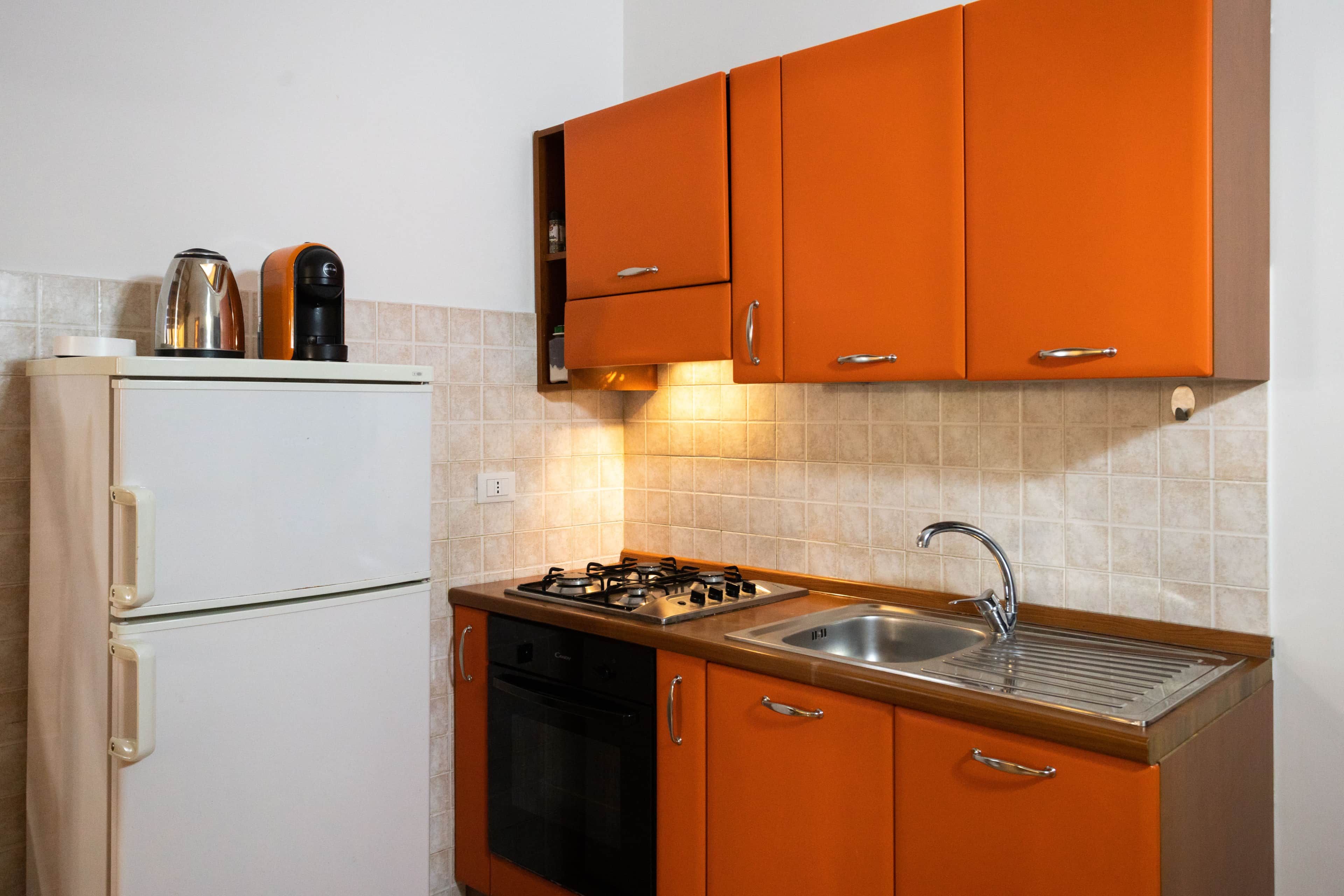 A compact kitchen with a refrigerator, stove, sink, and orange cabinets.