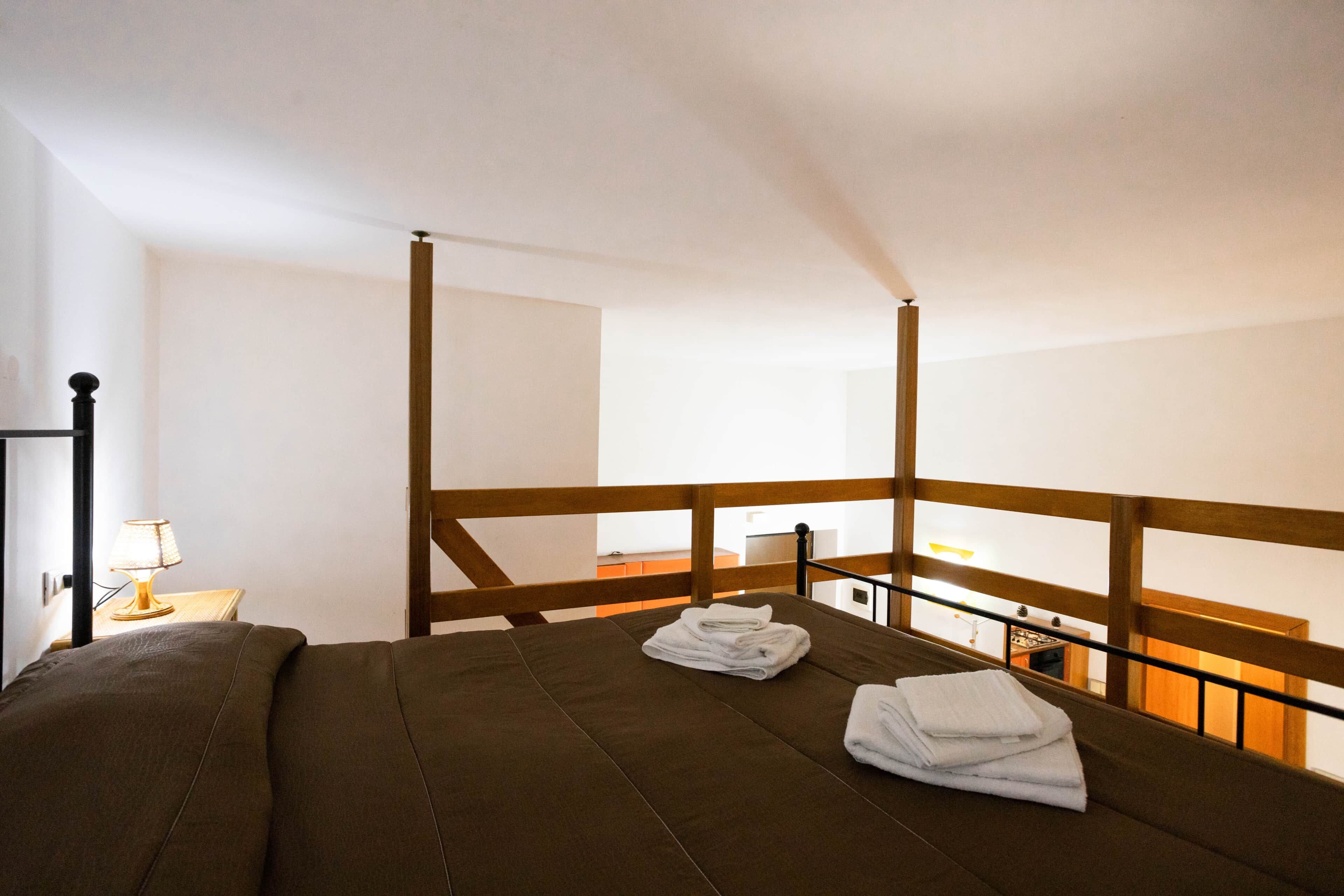A room with a bed, a nightstand, and a view of the kitchen.