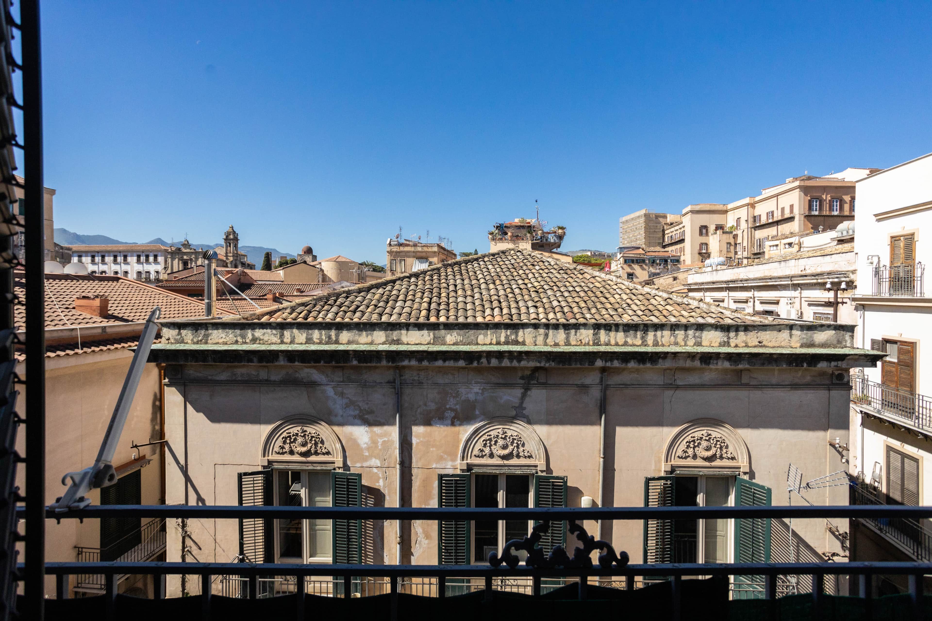 Un bâtiment doté d’un toit recouvert de tuiles, de nombreuses fenêtres avec volets et d’un balcon agrémenté de balustrades.