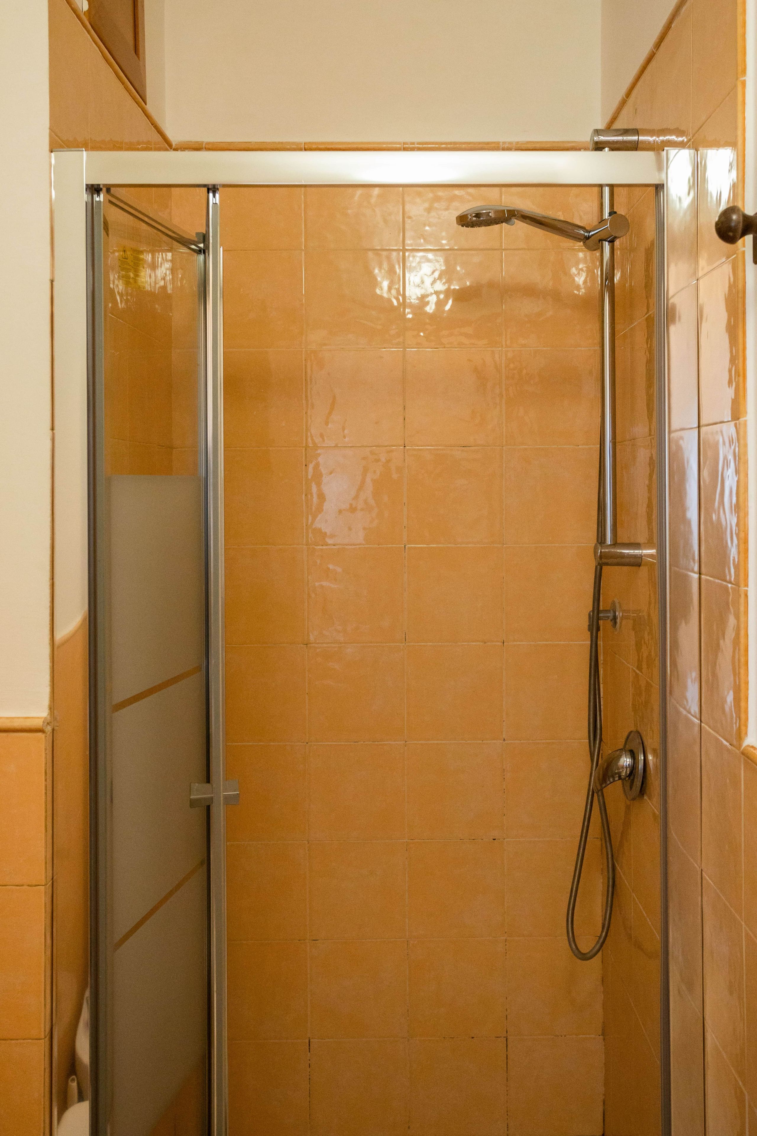 Une cabine de douche fermée par des parois en verre, dotée d’un pommeau de douche à main et d’un robinet mural.