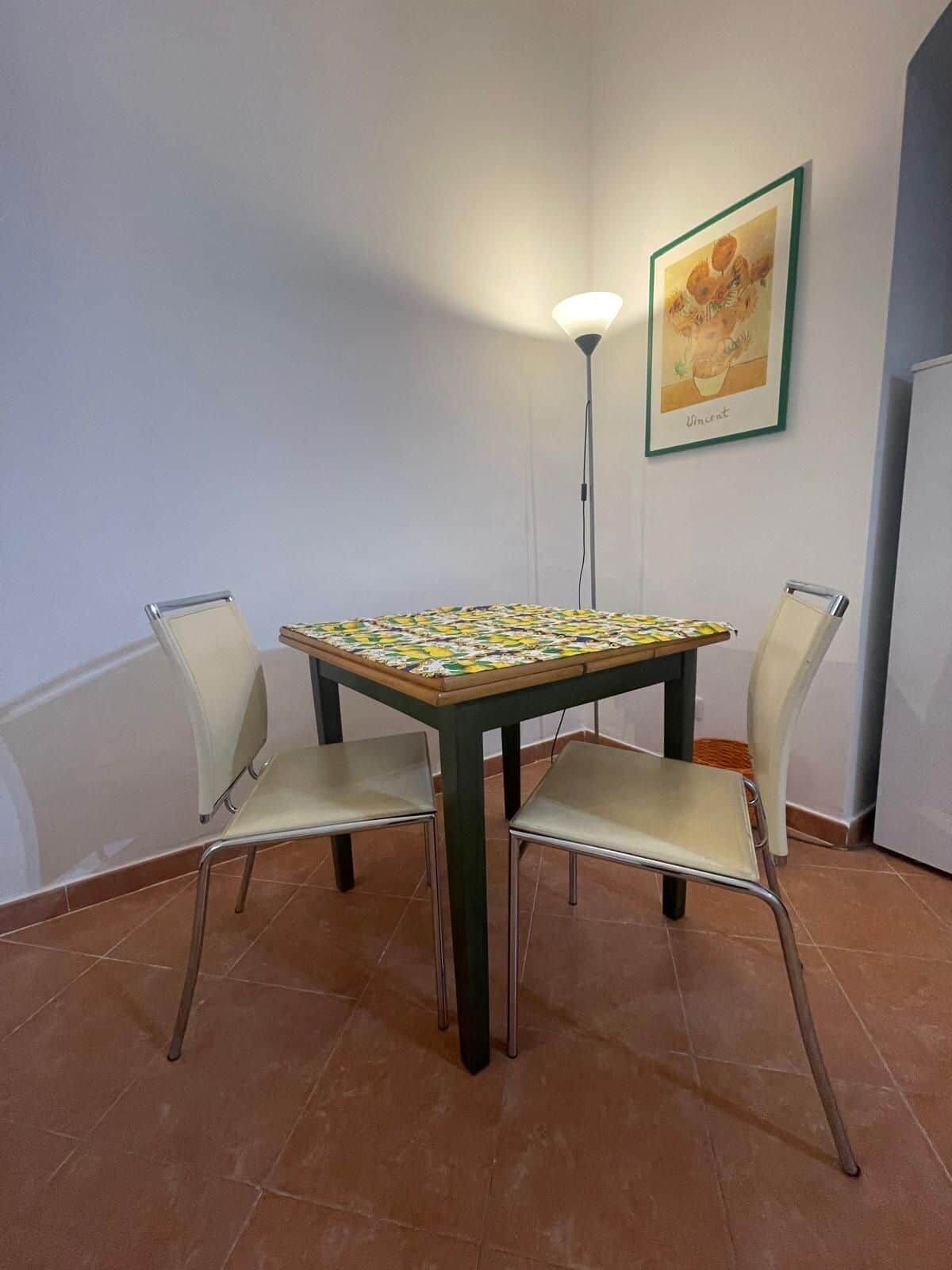 Une table à manger avec des chaises, un lampadaire et un tableau encadré au mur.