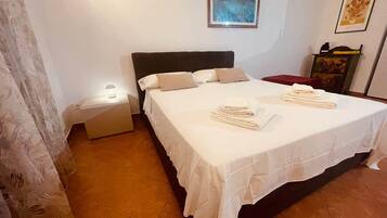 A neatly made bed with pillows and folded towels, a bedside table with a lamp, and artwork on the walls.
