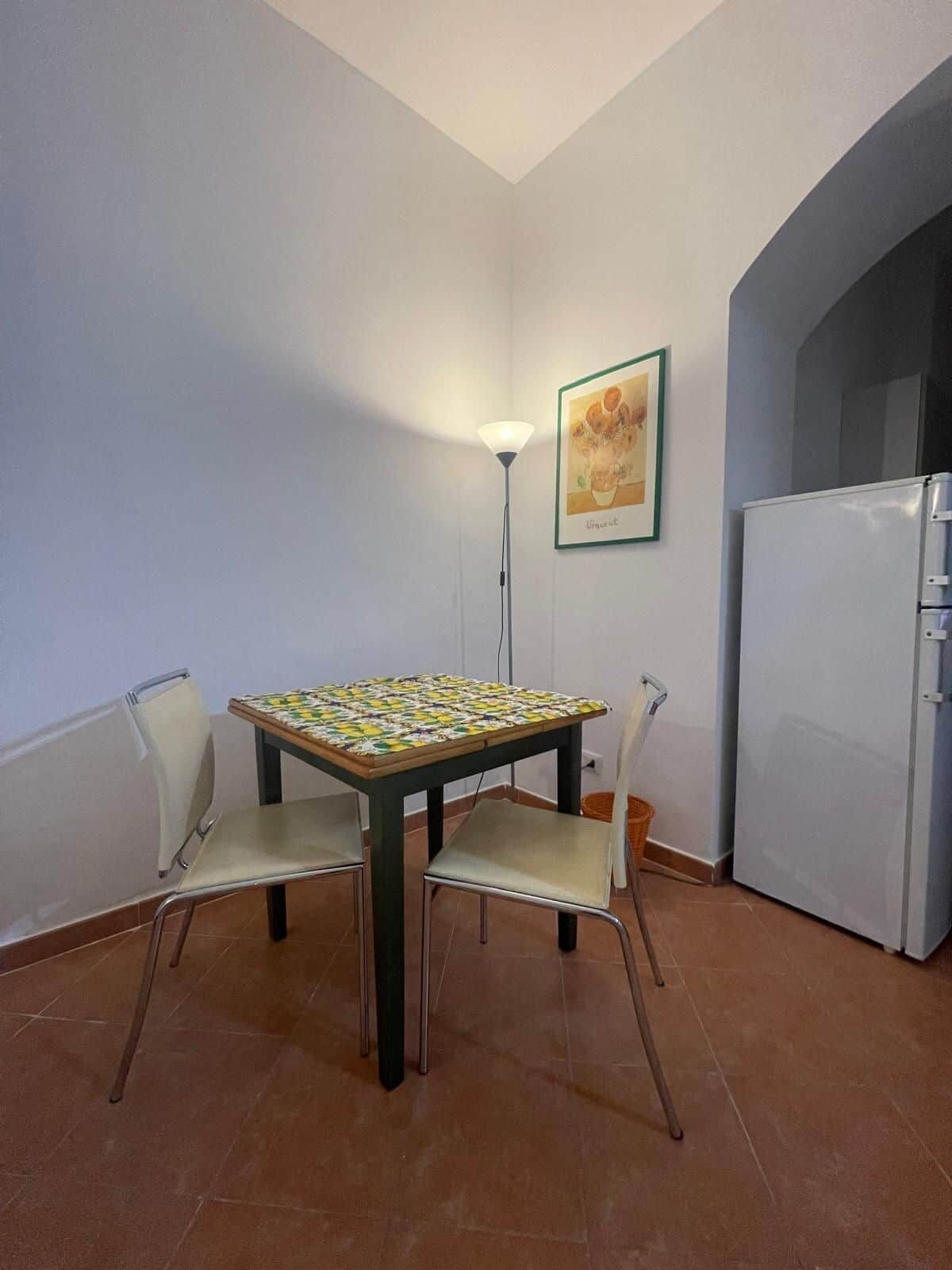 A dining area with a table and chairs, a refrigerator, and a floor lamp.