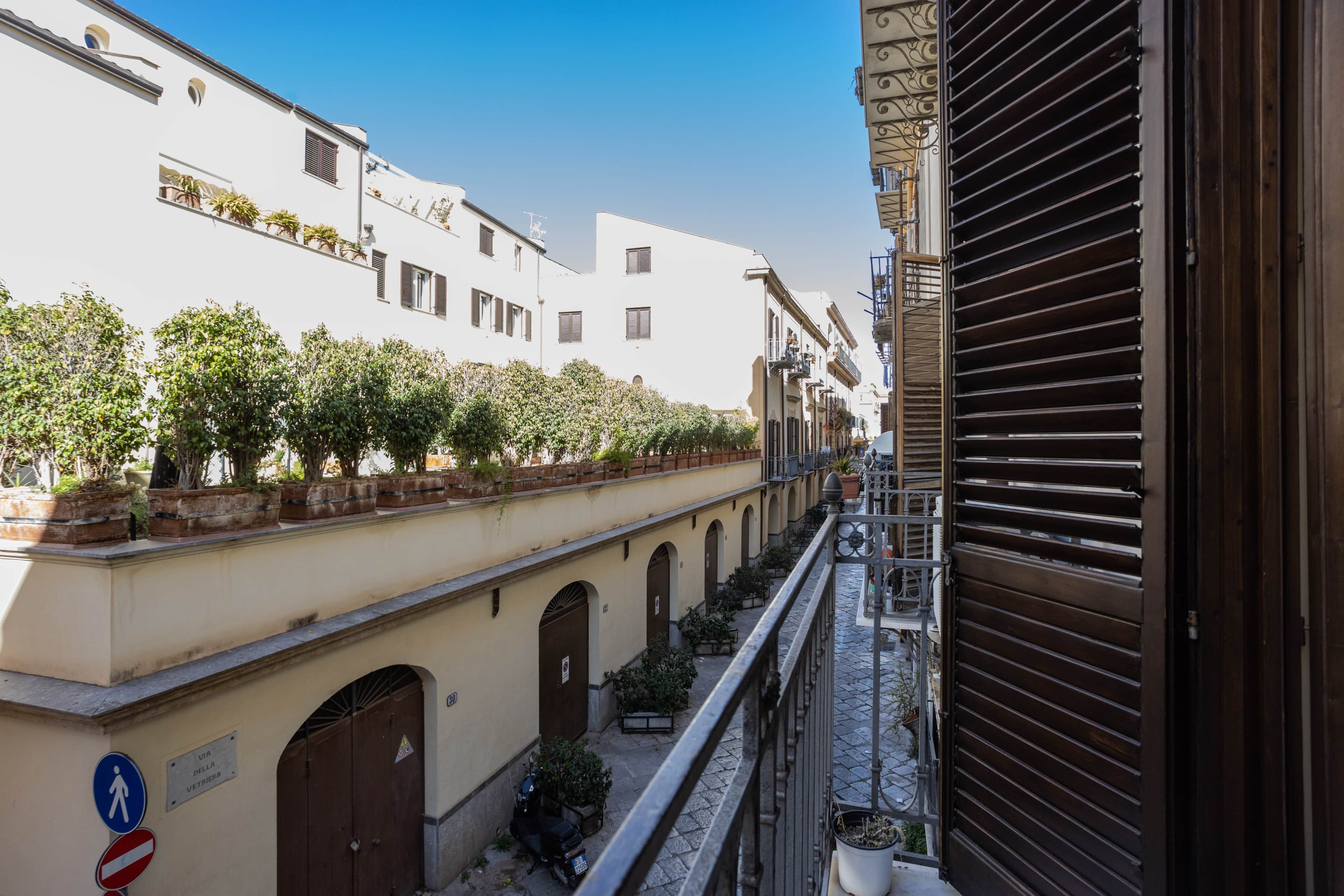 Une rue étroite, bordée de bâtiments des deux côtés, avec un chemin piétonnier et un volet fermé sur la droite.