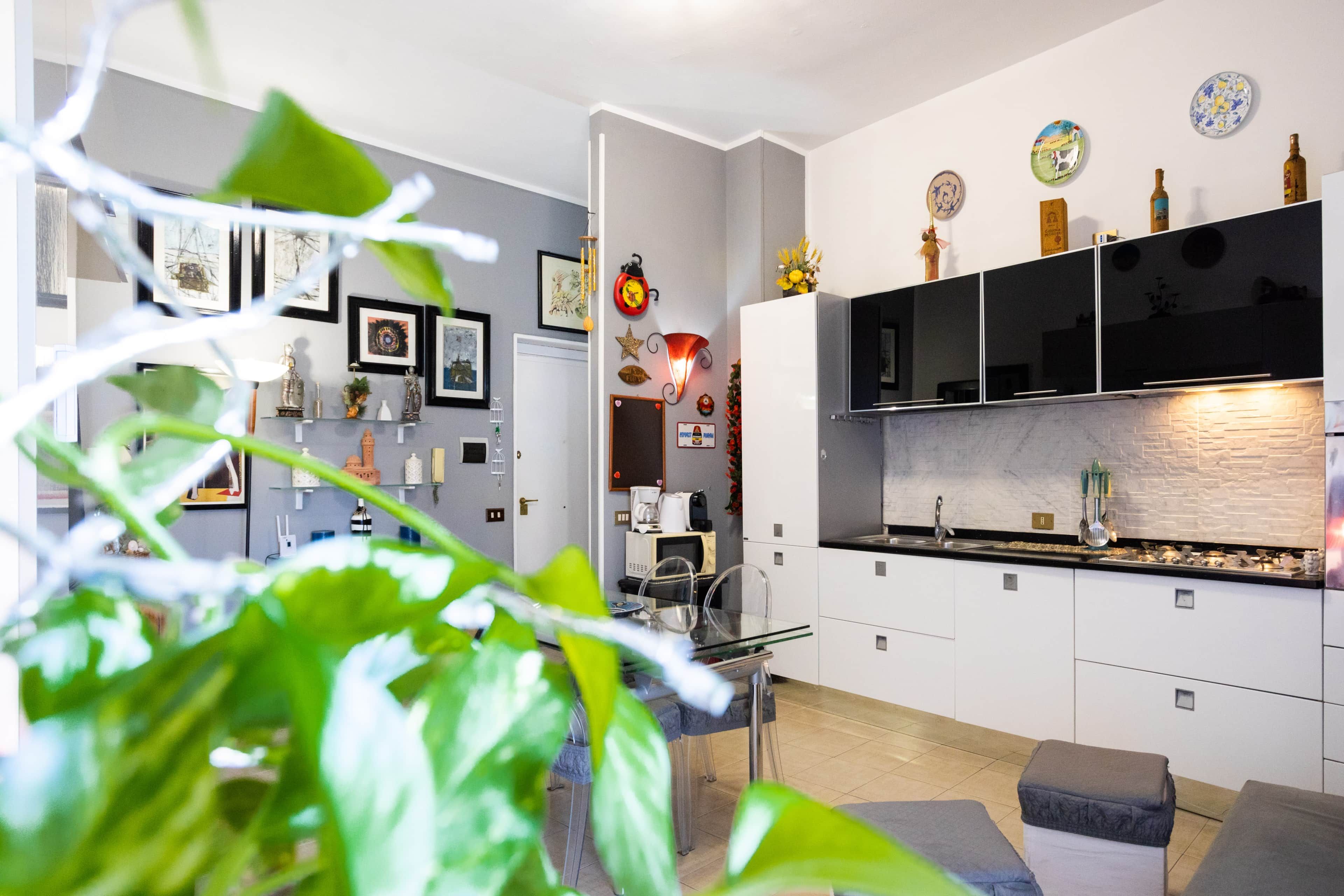 Une cuisine moderne avec des armoires blanches, un comptoir noir et un four encastré. On y trouve également un coin repas avec une table et des chaises en verre.