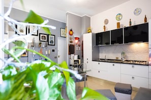 A modern kitchen with white cabinets, a black countertop, and a built-in oven. There is a dining area with a glass table and chairs. - Hola Cathedral House Porta di Castro (Palermo)