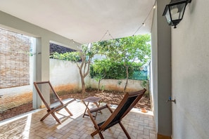 A covered patio with two wooden chairs, a small table, and a hanging light fixture. - Hola House Mondello Addaura (Palermo)