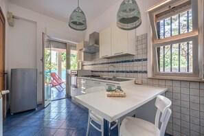 A kitchen with a central island, a refrigerator, and a window with bars. - Hola House Mondello Addaura (Palermo)
