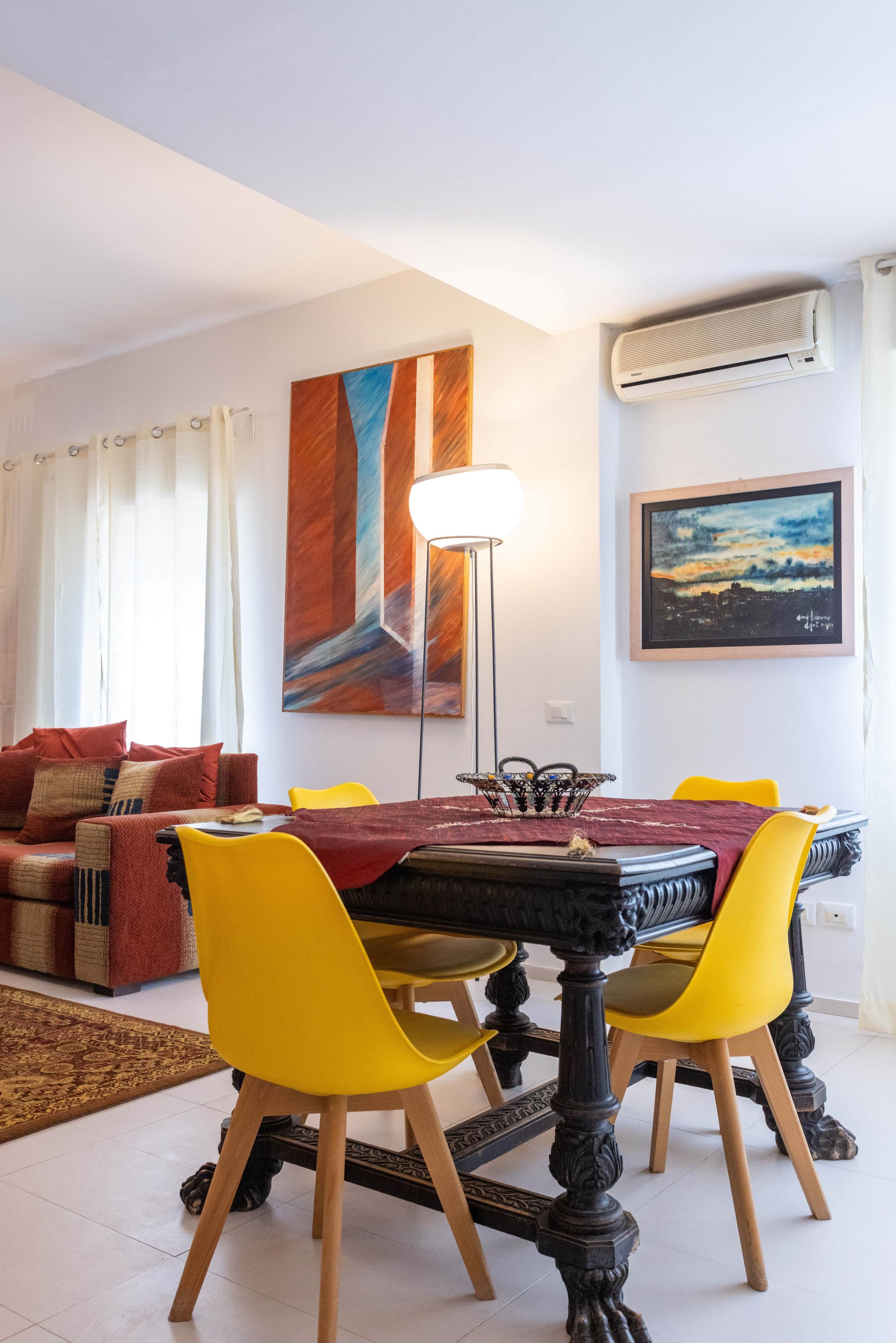 Un coin repas avec une table ronde, des chaises jaunes et une lampe moderne.