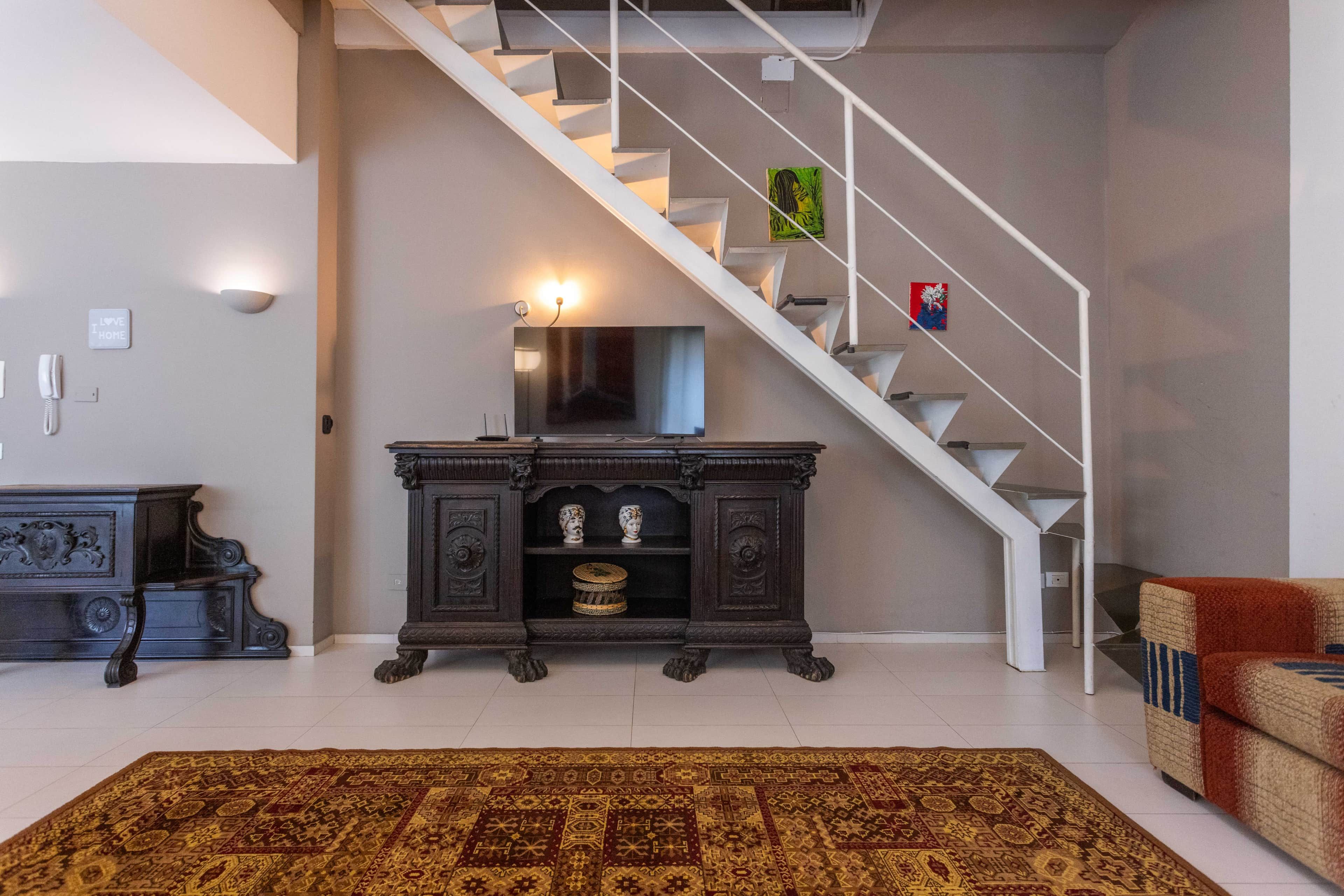 Eine moderne Treppe, ein an der Wand befestigter Flachbildfernseher und eine dunkle Holzeinrichtung mit Dekorationsgegenständen.