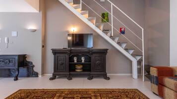 Un escalier au design moderne, un téléviseur à écran plat fixé au mur et un meuble en bois foncé agrémenté d’objets décoratifs.