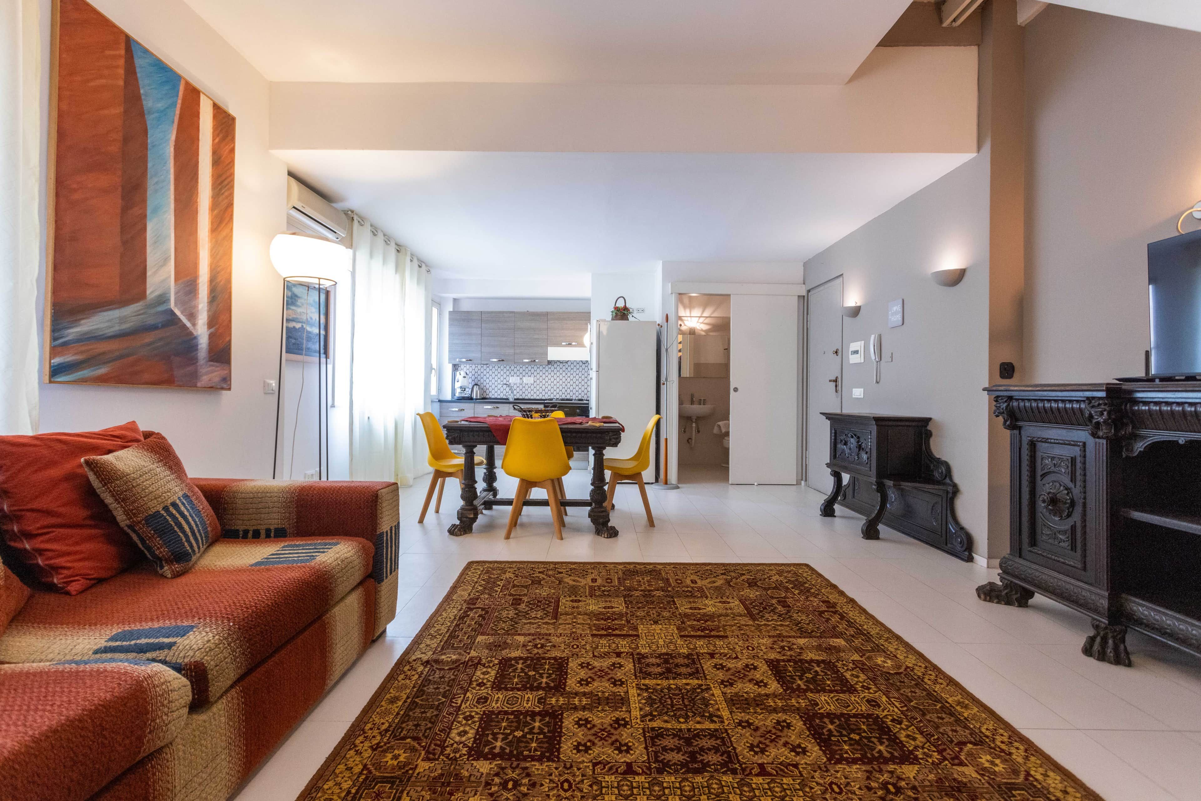 Un salon moderne avec un canapé, une table à manger et des chaises, un tapis à motifs et un téléviseur.