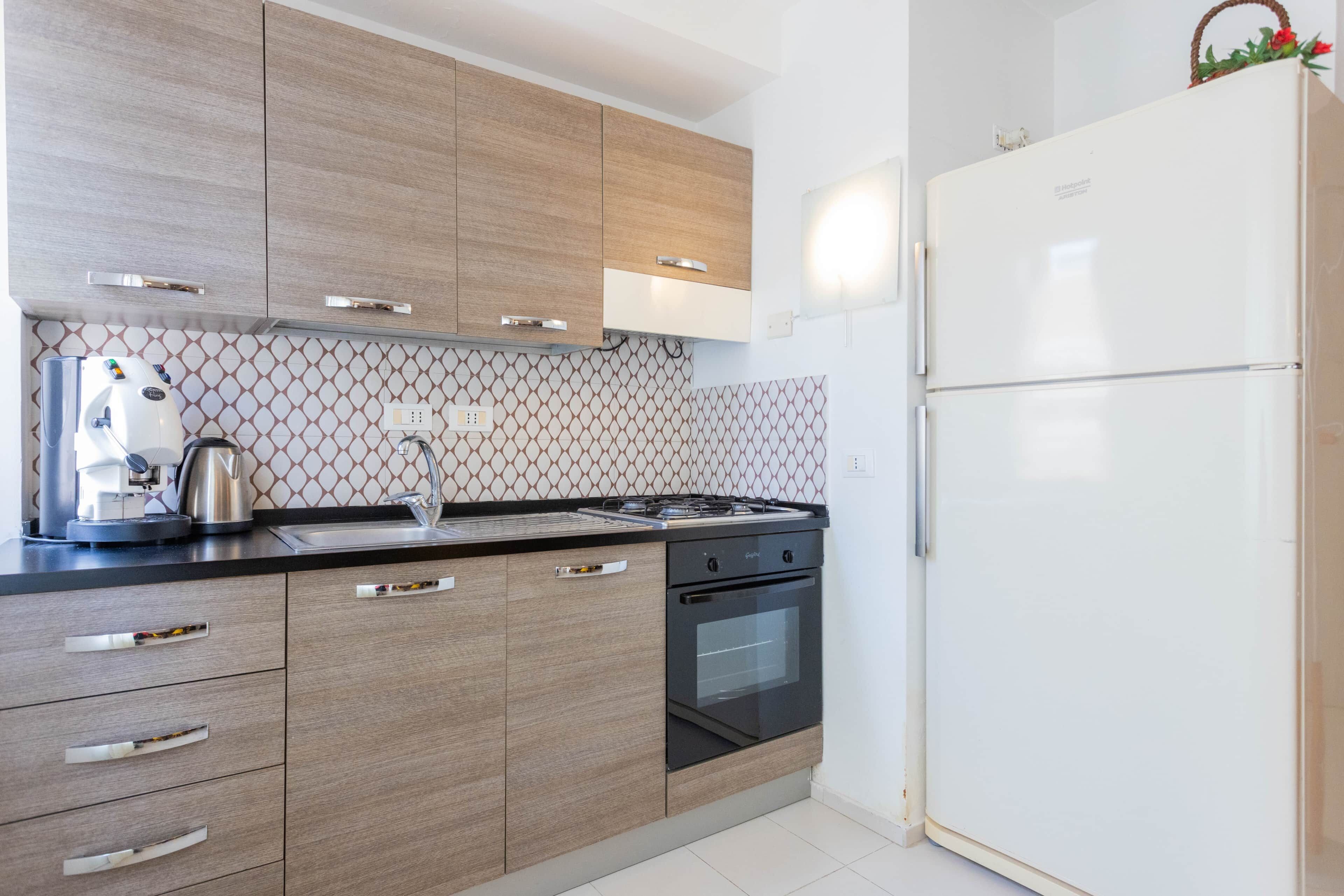 Une cuisine moderne avec des meubles en bois, une cuisinière à gaz, un four encastré et un réfrigérateur blanc.
