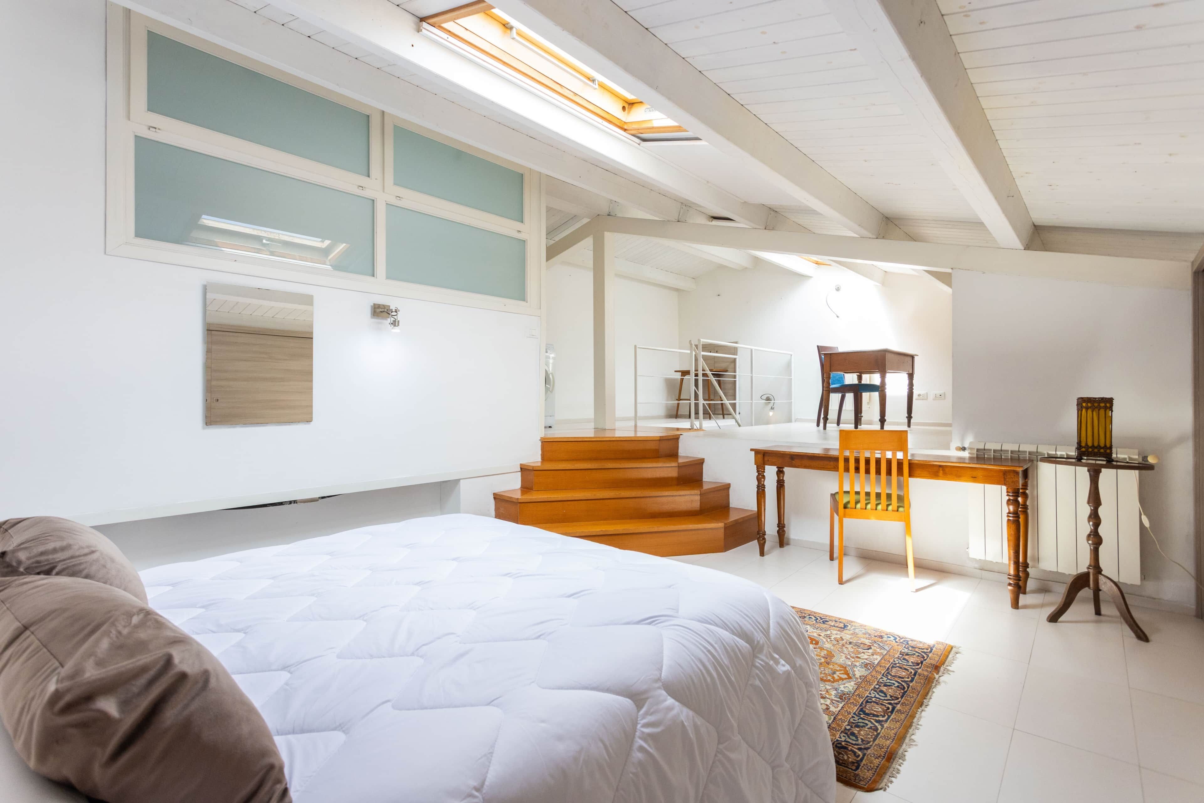 Une chambre à coucher avec un lit, un bureau et une chaise. Un escalier mène à un étage supérieur.