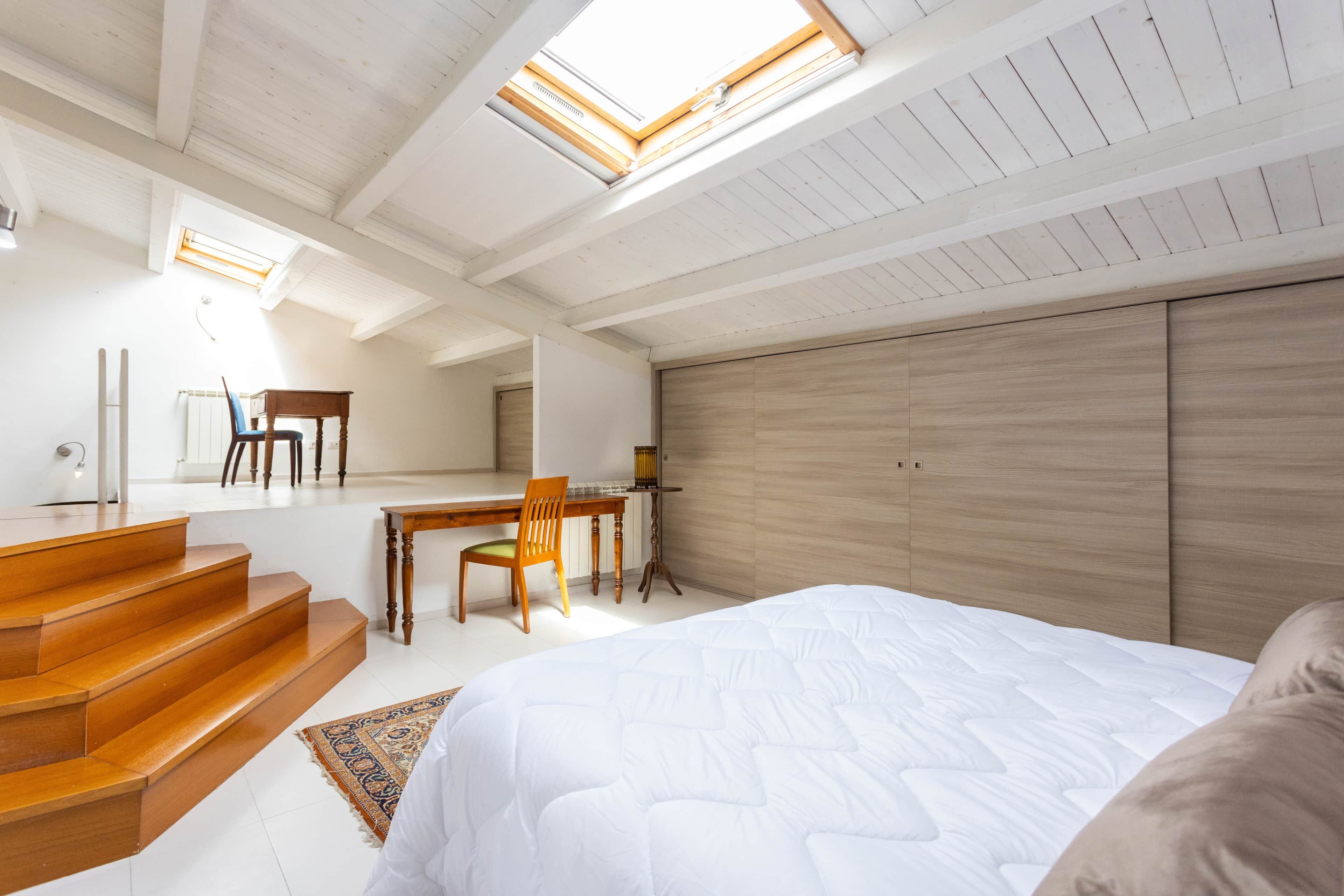 A bedroom with a bed, wooden staircase, a desk, and a chair.