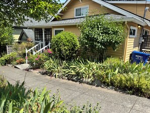 Une maison d’habitation avec un jardin devant, un escalier et une poubelle bleue pour le recyclage.