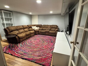 A corner living room with a sectional sofa, a patterned rug, a white cabinet, and a TV mounted on the wall. - Walkable Top of Queen Anne 5BR + Parking (Seattle)