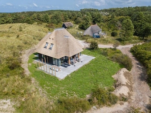 A modern house with a thatched roof, surrounded by a grassy landscape and a forested hill. - Luxury Dune Villa With Sauna for 8 in Ameland (Buren)