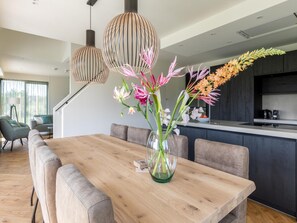A modern dining area with a wooden table and cushioned chairs, a vase with flowers, and pendant lights. - Luxury Dune Villa With Sauna for 8 in Ameland (Buren)