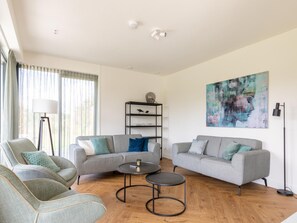 Ein modernes Wohnzimmer mit zwei grauen Sofas, einer Stehlampe, einem Bücherregal und einem Bild an der Wand.
