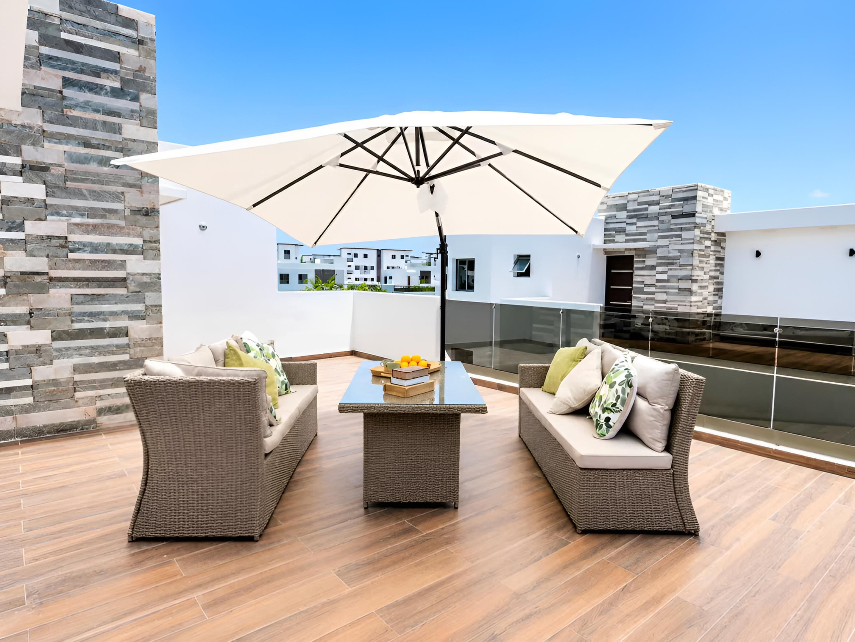 A rooftop terrace with wicker furniture, a table with fruit, and a large umbrella.