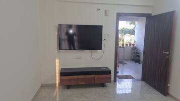 Une pièce dotée d’un téléviseur à écran plat fixé au mur, d’un meuble en bois en dessous et d’une porte donnant sur un espace extérieur agrémenté de plantes en pot.
