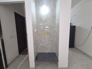 Un bany amb zona de dutxa, una porta blanca i una paret de marbre.