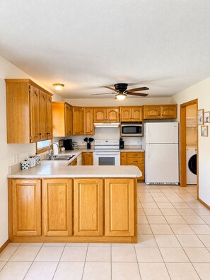 A kitchen with wooden cabinets, a central island, a microwave, a refrigerator, and a ceiling fan.