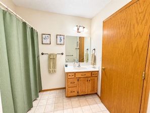 A bathroom with a wooden vanity, a mirror, a towel rack, and a green shower curtain.