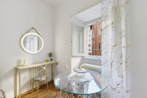 Ein Zimmer mit einem runden Spiegel, einem kleinen Tisch mit einer Vase, einem Stuhl und einem Glastisch mit einem weißen, flauschigen Gegenstand.