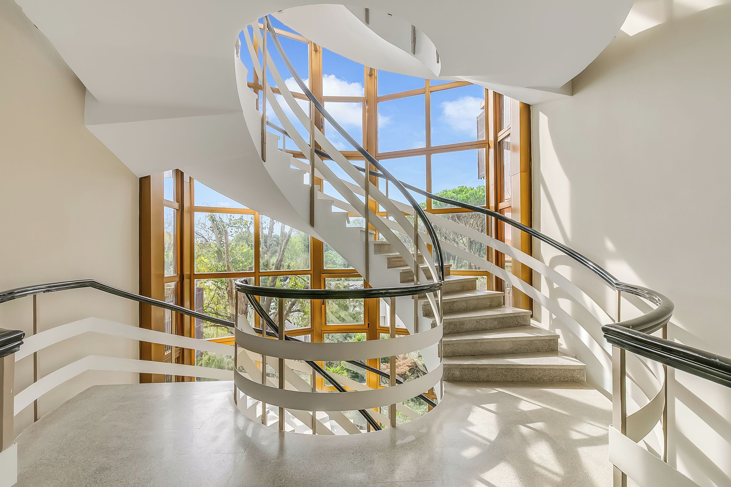 Un escalier en colimaçon avec une rampe en verre, menant à l’étage supérieur.