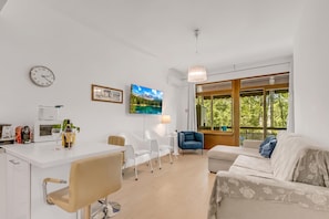 A modern living room with a white sofa, a dining area with a white table, and a large window with a view of trees. - Park Apt With AC & Private Balcony, 300 mt to Sea (Viareggio)