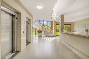 Eine Hotelhalle mit einer Rezeption, einer Treppe, die zu einem Außenbereich führt, und einem großen Fenster mit Blick auf Grünflächen.