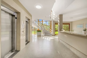 A hotel lobby with a reception desk, a staircase leading to an outdoor area, and a large window with a view of greenery. - Park Apt With AC & Private Balcony, 300 mt to Sea (Viareggio)