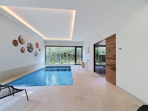 A modern indoor swimming pool with a clear view of the outdoors, a ceiling with recessed lighting, and a series of decorative wall art. - Family Retreat in Belgium With Sauna (Rochefort)