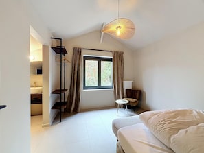 A bedroom with a bed, a window with curtains, a hanging light fixture, and a chair. - Family Retreat in Belgium With Sauna (Rochefort)