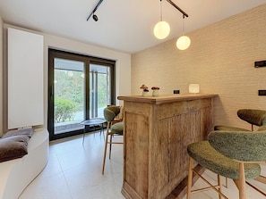 A modern interior with a wooden bar, seating area, and a large window offering a view of greenery. - Family Retreat in Belgium With Sauna (Rochefort)