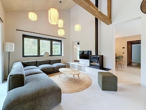 A modern living room with a sectional sofa, a TV, and a fireplace. - Family Retreat in Belgium With Sauna (Rochefort)