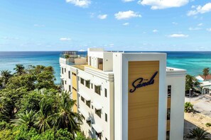 A hotel with a prominent sign reading 'The Sands,' featuring a modern architectural style with multiple floors and balconies overlooking a coastal view. - The Sands #5 (Seven Mile Beach)