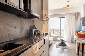 A modern kitchen with a black countertop, a built-in oven, and a coffee machine. There is a large window with a view of the city. - EK SkySuite Altura Upperhill Floor 21 with Panoramic views (Nairobi)