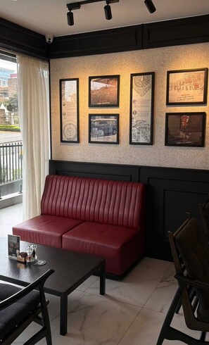 Un canapé rouge, une table et des chaises dans une pièce dont les murs sont ornés de tableaux encadrés.