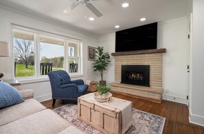 Ein Wohnzimmer mit Kamin, blauem Sessel, Sofa und großem Fenster.