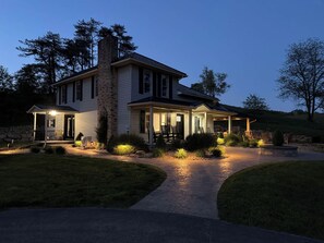 Ein zweigeschossiges Haus mit überdachter Veranda, einem Stein-Schornstein und einem angelegten Vorgarten.