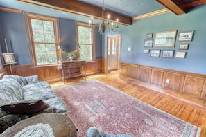 A spacious room with wooden floors, a large window, a chandelier, and a collection of framed pictures on the wall. - Historic Gettysburg B&B - Queen Room - Private Bath - Hot Tub & Sauna (Gettysburg)
