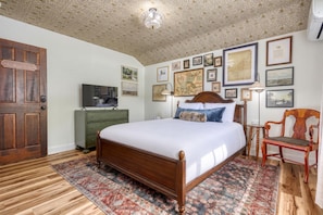 A bedroom with a wooden bed, a green dresser, a television, and a wall adorned with framed pictures. - Historic Gettysburg B&B - Queen Room - Private Bath - Hot Tub & Sauna (Gettysburg)